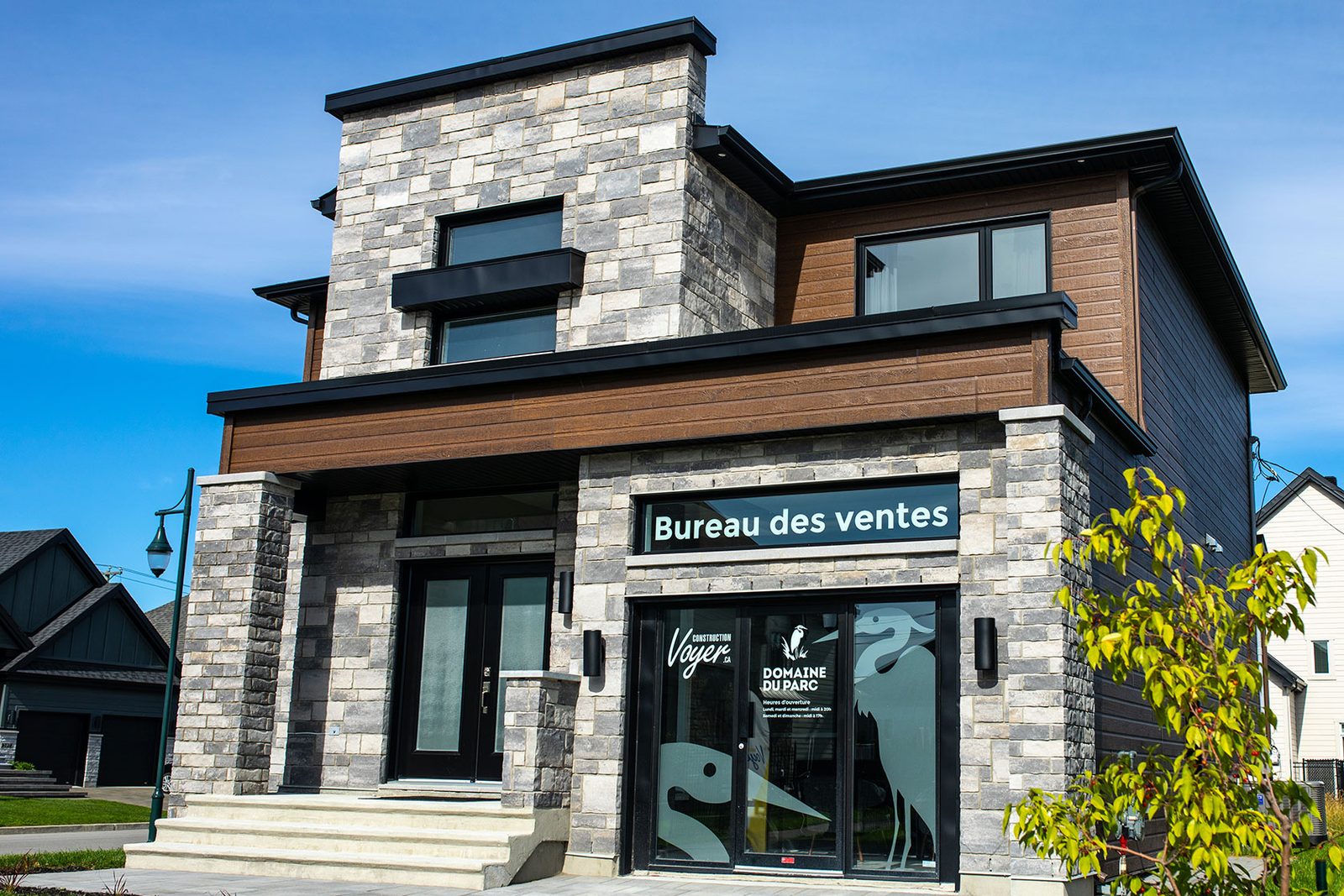 Un bureau des ventes de Construction Voyer : pierre grise, bois et grandes fenêtres noires